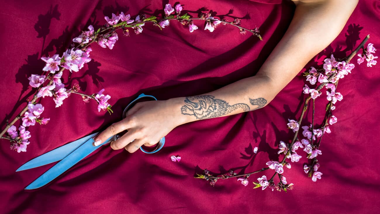 womans arm with wolf tattoo holding scissors surrounded by flowers